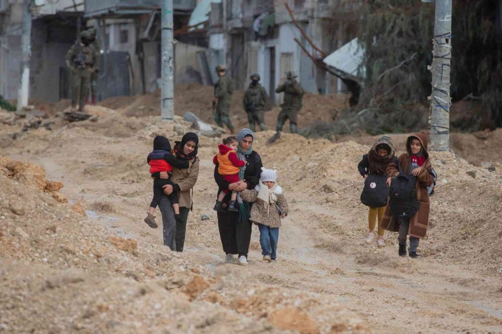 Um grupo de mulheres e crianças caminha por um caminho lamacento no campo de refugiados de Nur Shams, a 10 de fevereiro de 2025. Chuvas fortes pioraram as condições no campo, que já enfrentava dificuldades nas deslocações e com infraestruturas limitadas. (Foto de WAHAJ BANI MOUFLEH/Middle East Images/AFP via Getty Images)